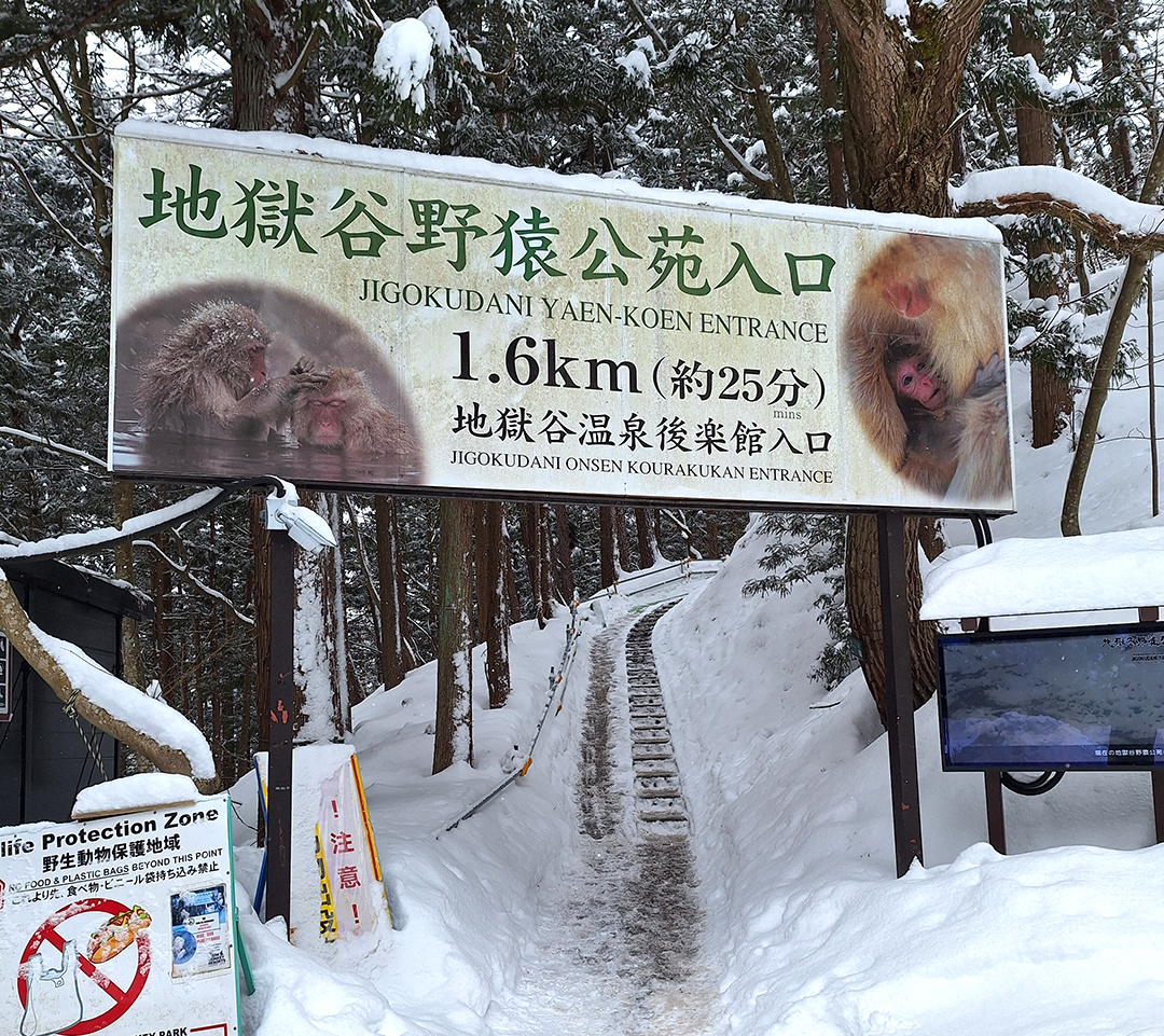 Entrance sign for Jigokudani Yaen-Koen Snow Monkey Park in a snowy Japanese landscape