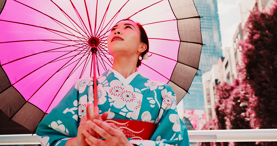 Woman wearing a traditional Japanese kimono with a pink paper umbrella.