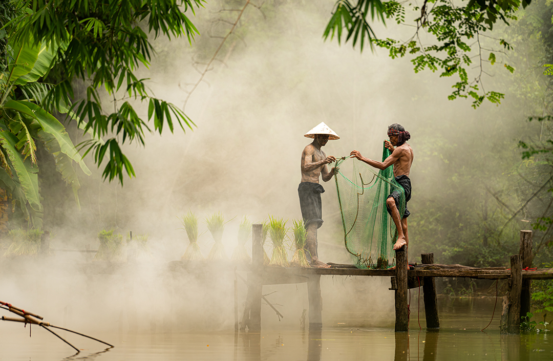 Two fishermen preparing a fishing net beside a river in the tropical landscape of the Philippines.