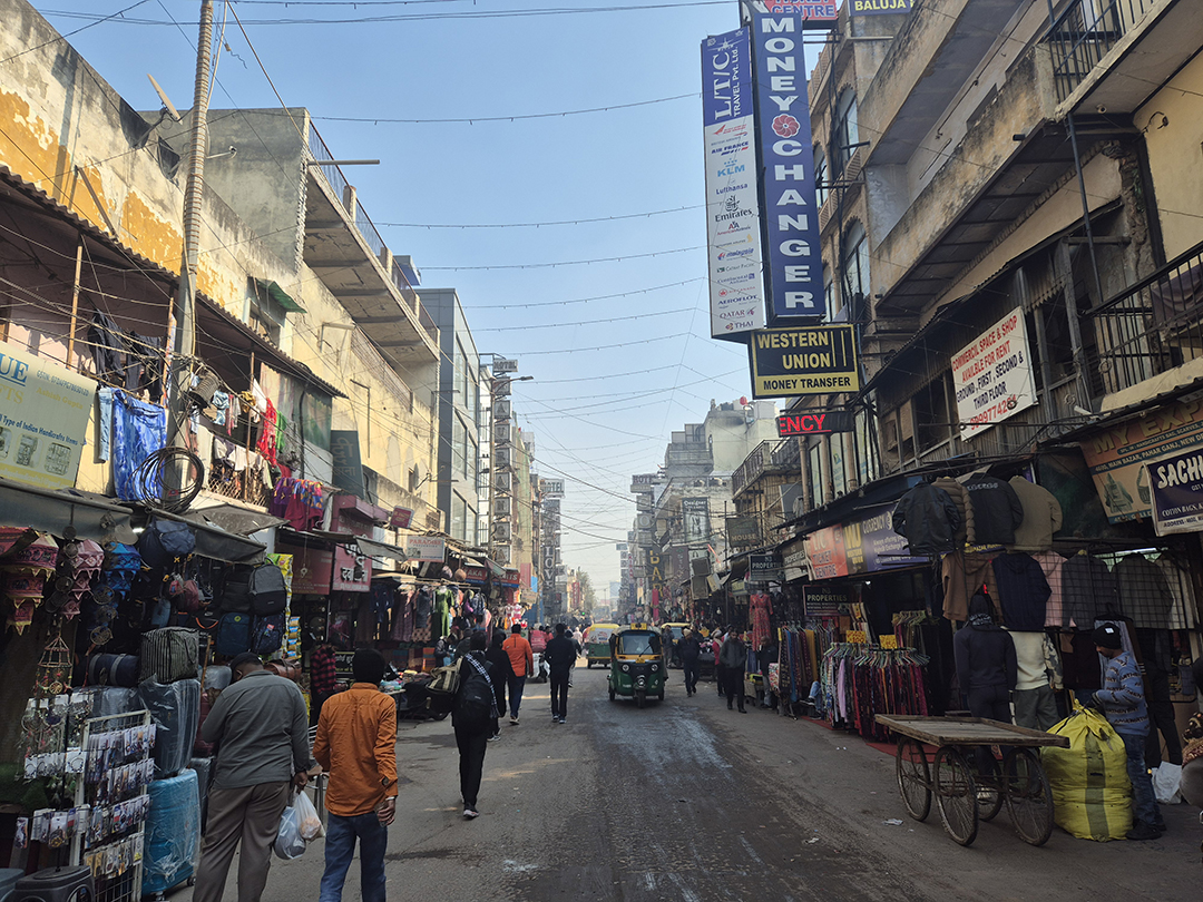 Street in Old Delhi with bustling shops, a rickshaw and everyday city life.