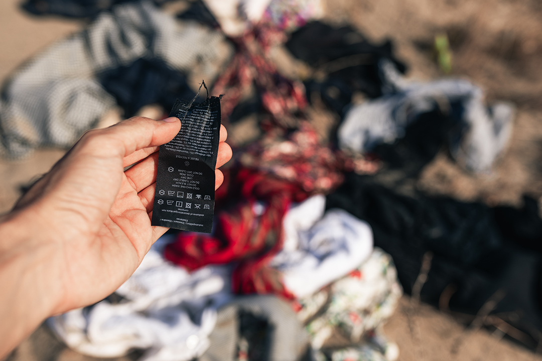 A clothing label held in front of discarded textiles highlights the growing problem of textile waste caused by the fast fashion industry.